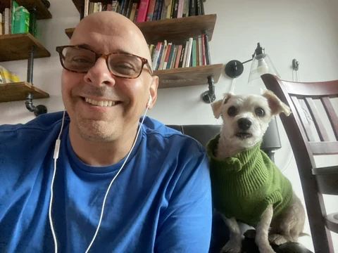 Rumi in a green sweater sitting beside his owner